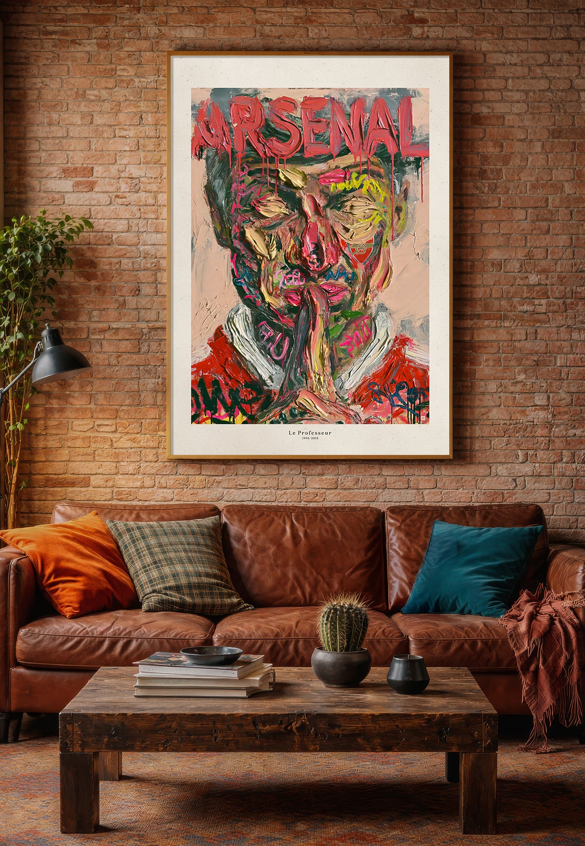Arsenal-kunsttrykket Le Professeur med Arsène Wenger, vist i treramme på murvegg over en brun skinnsofa.